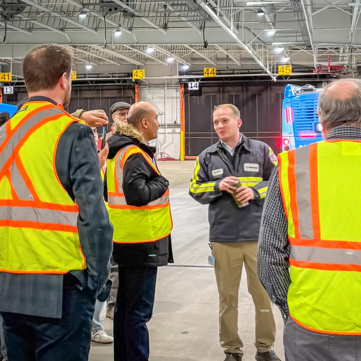 A photo of an STA staff talking to visitors wearing safety vests while standing in an STA bus garage