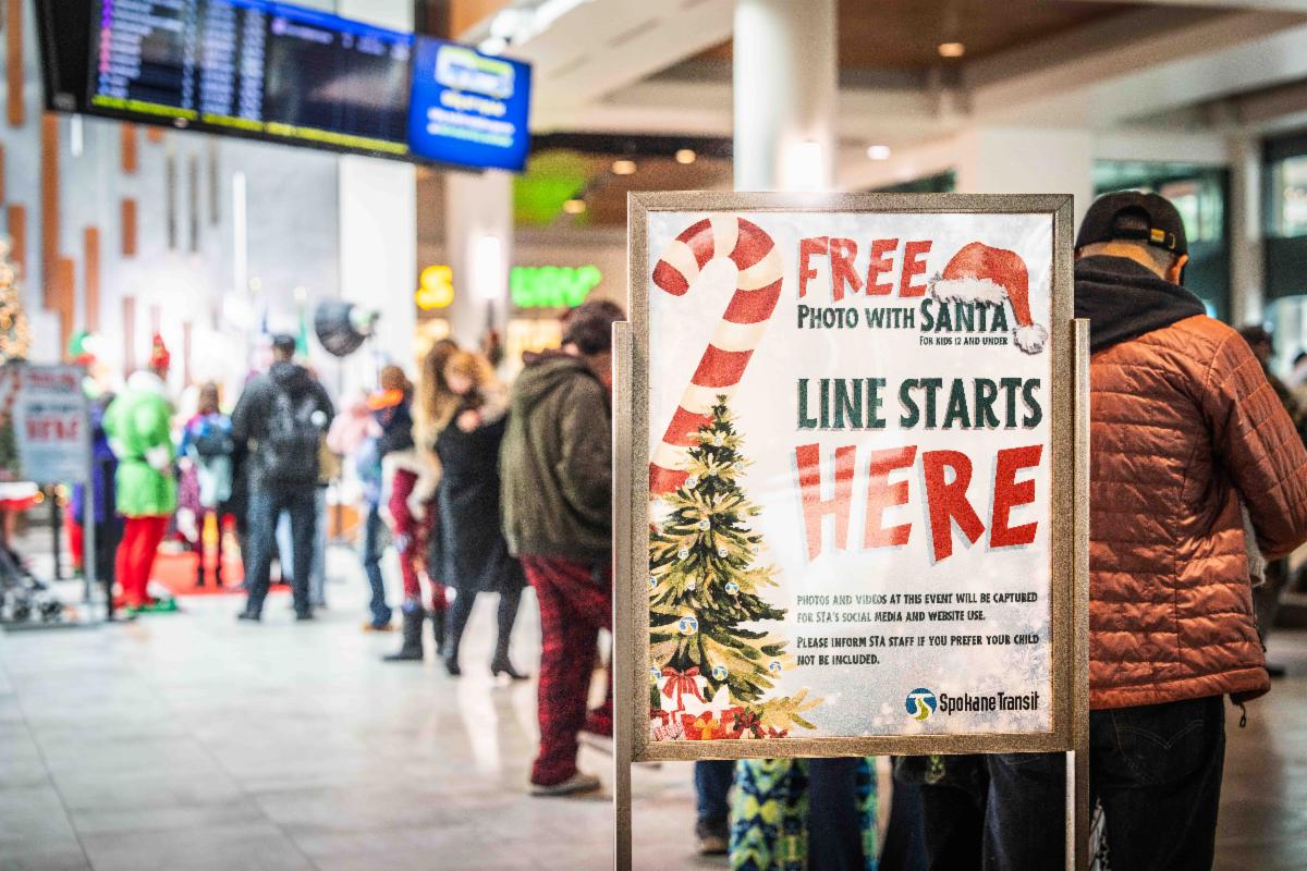 A photo of the welcome sign for the Santa Photo event and a line of people waiting to have their Santa photos taken