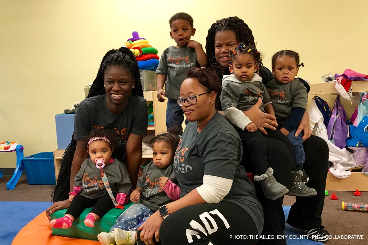 Young children sitting with their caretakers all smiling.