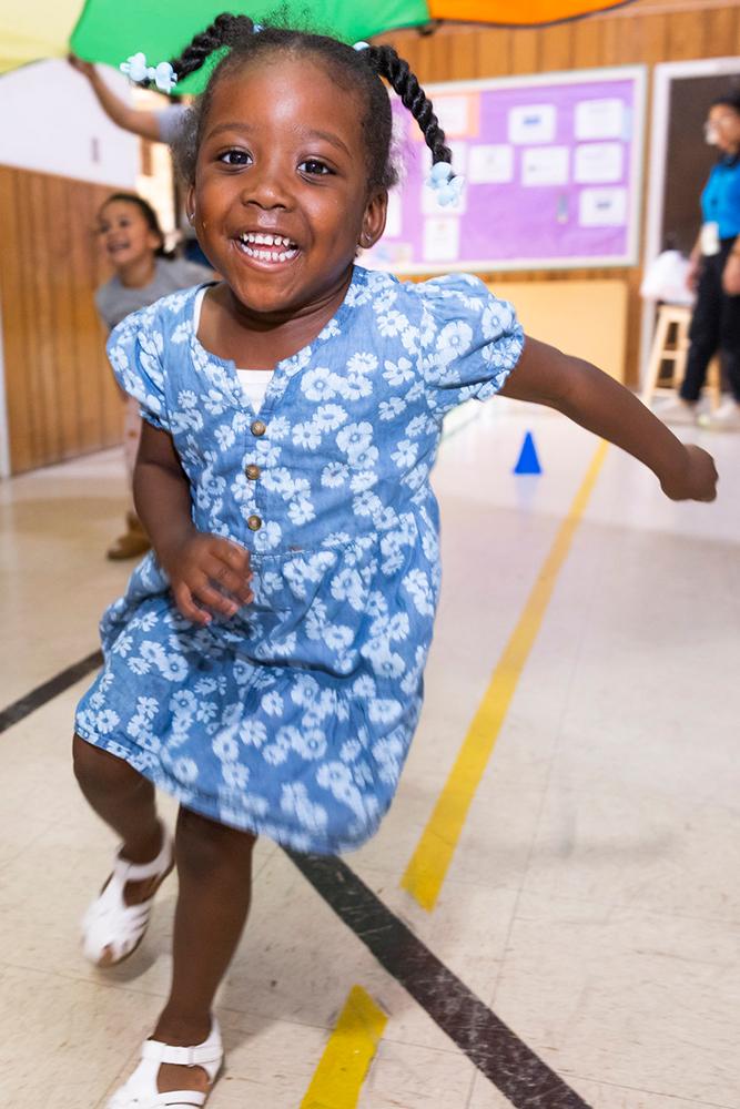 Young girl running in gymnasium smiling.