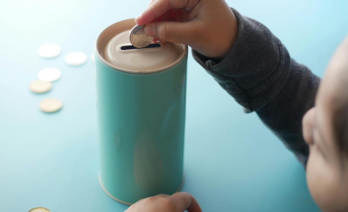 Child dropping coins in piggy bank.
