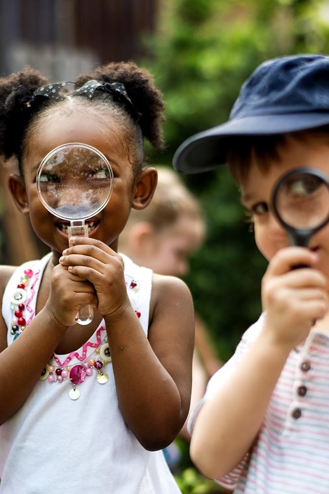 Playful children looking through magnifying glasses at the camera.