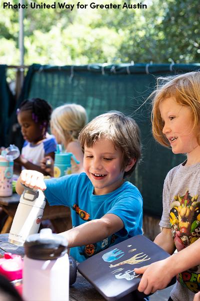 Pairs of kids at picnic tables outdoors.