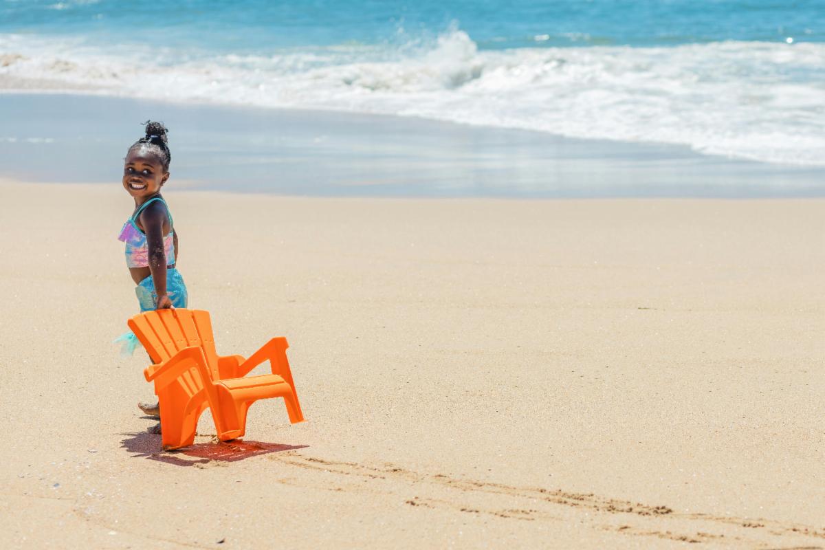 Little girl pulling a chair on the beach.