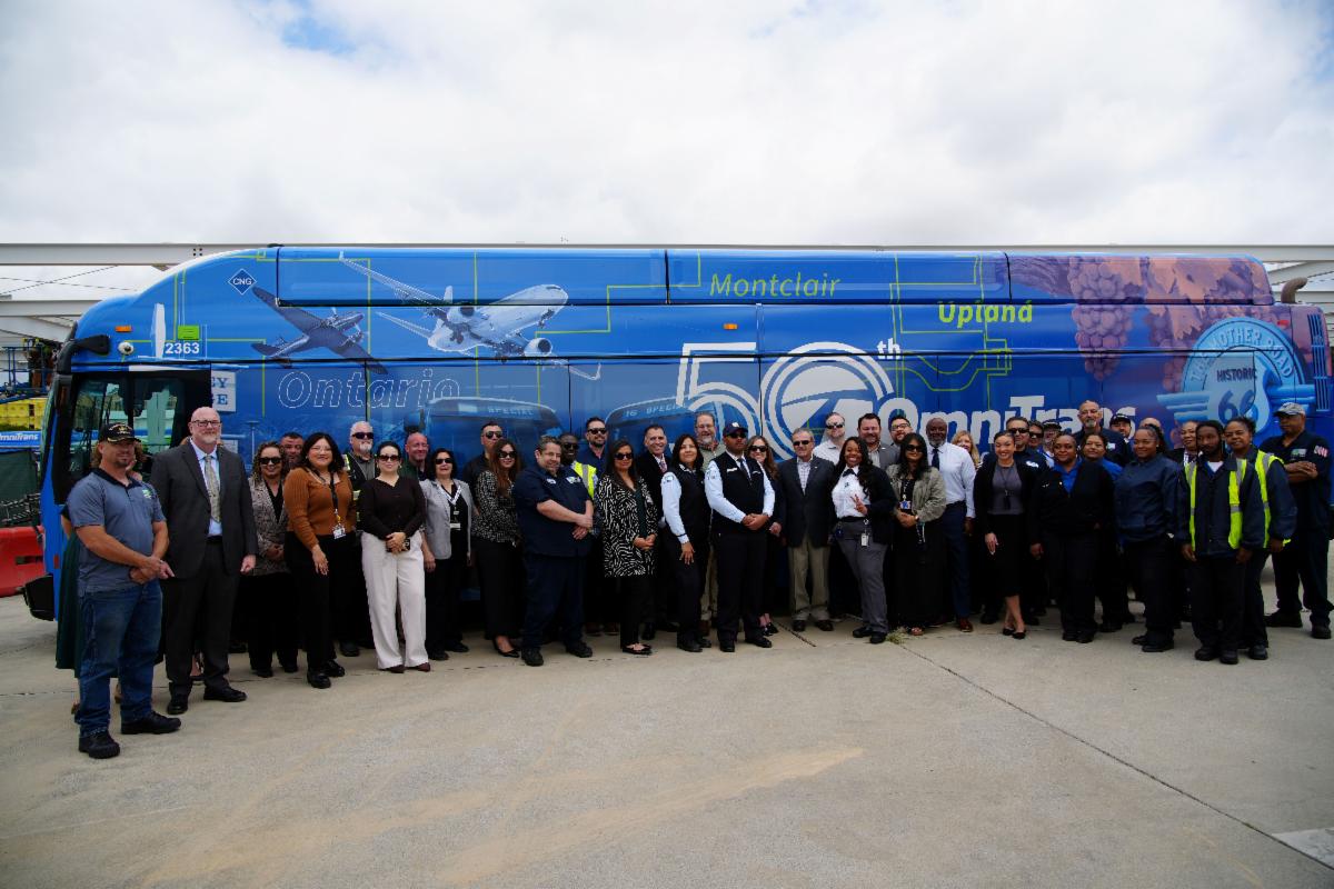 ONT shuttle wrapped in 50th anniversary design, in front of shuttle is a group of employees, stakeholders, and dignitaries. 