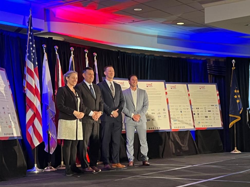 Four people standing on a stage with flags posing for a picture.