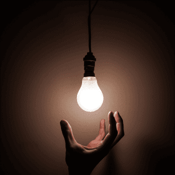 Hand reaching toward lightbulb in a dark room