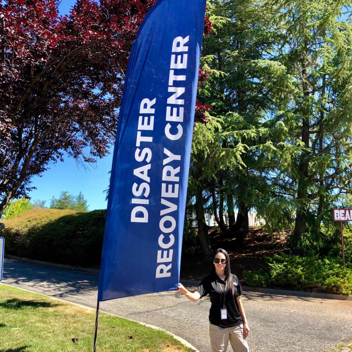 A person stands next to a tall blue flag that reads Disaster Recovery Center