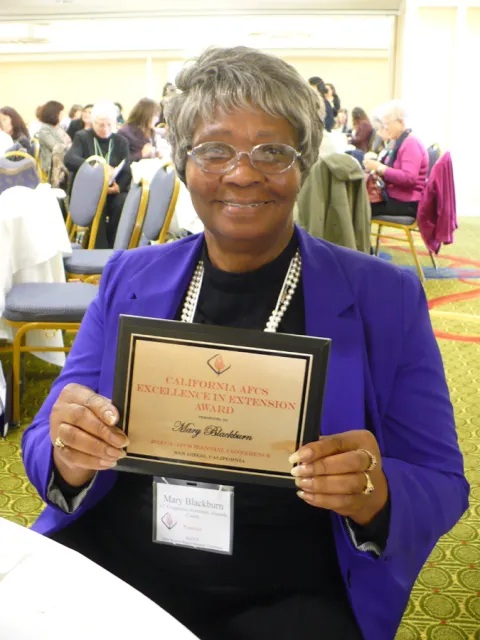Mary Blackburn smiles while holding up American Association of Family and Consumer Sciences Extension Excellence Award