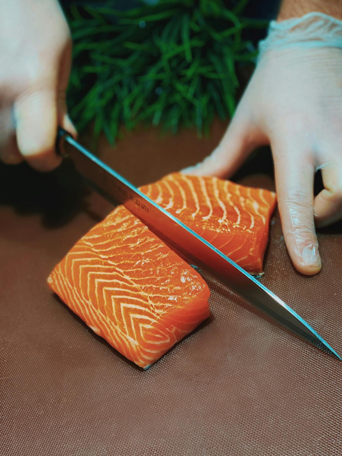 Person slices into a salmon fillet with a sharp knife