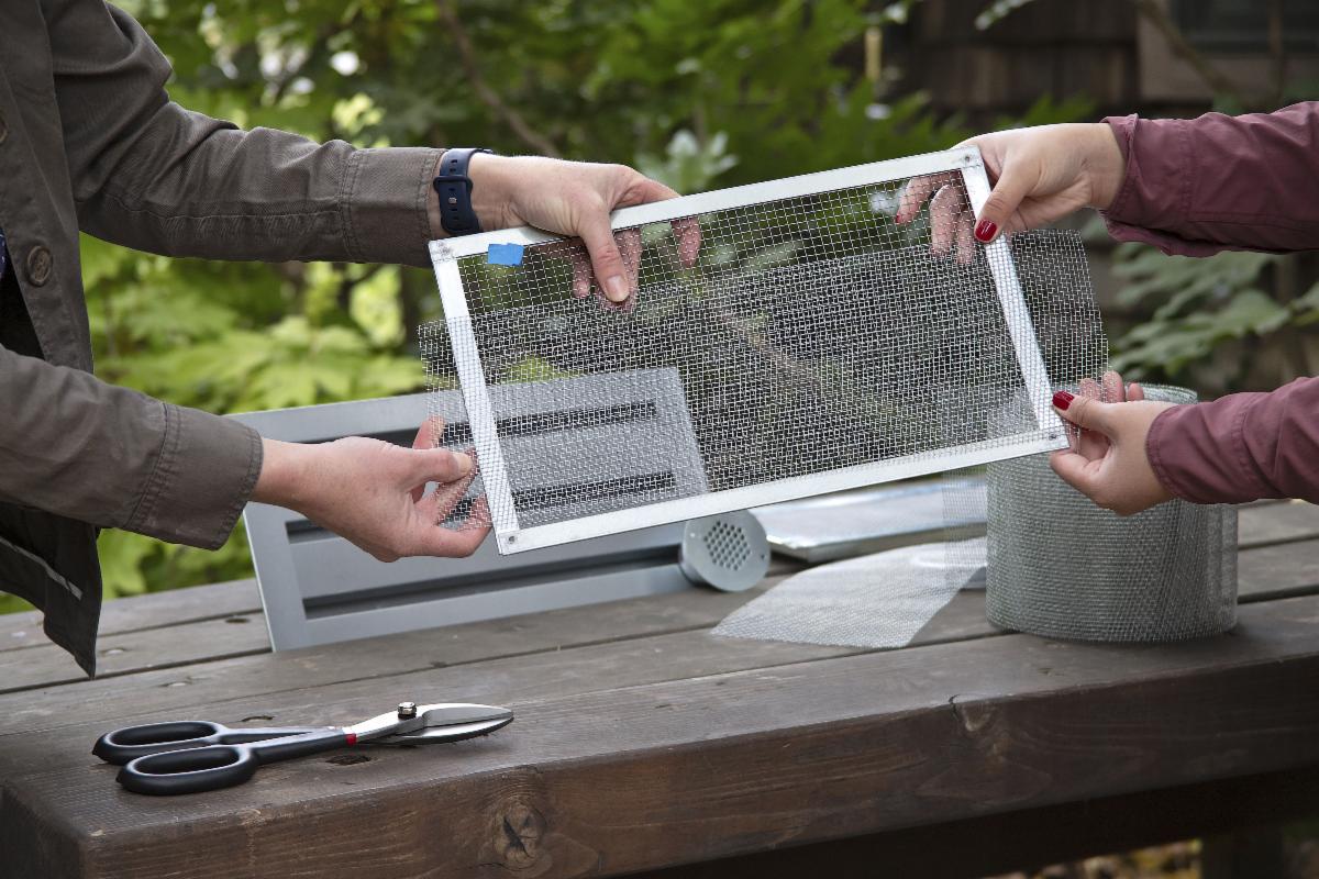 Two pairs of hands hold a fine mesh screen that should be used to keep fire embers out