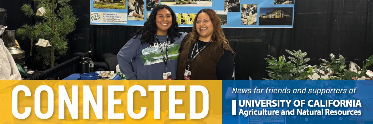 Two women smile as they pose behind their booth at the World Ag Expo