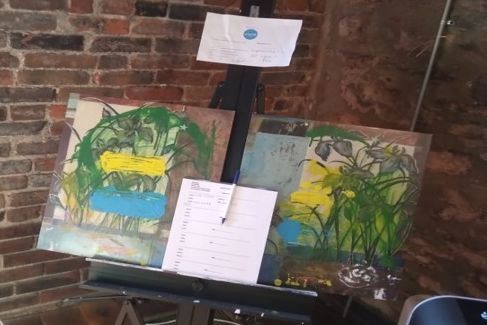 art easel with two original works of art displayed in a studio space with exposed brick walls