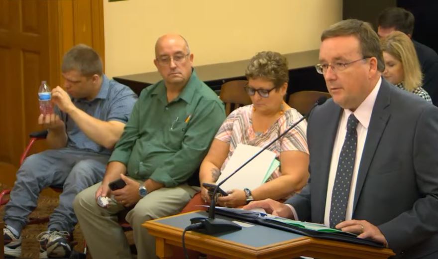 image contains a gallery room in the Topeka Capitol Building with members of the public sit listening to testimony about KanCare