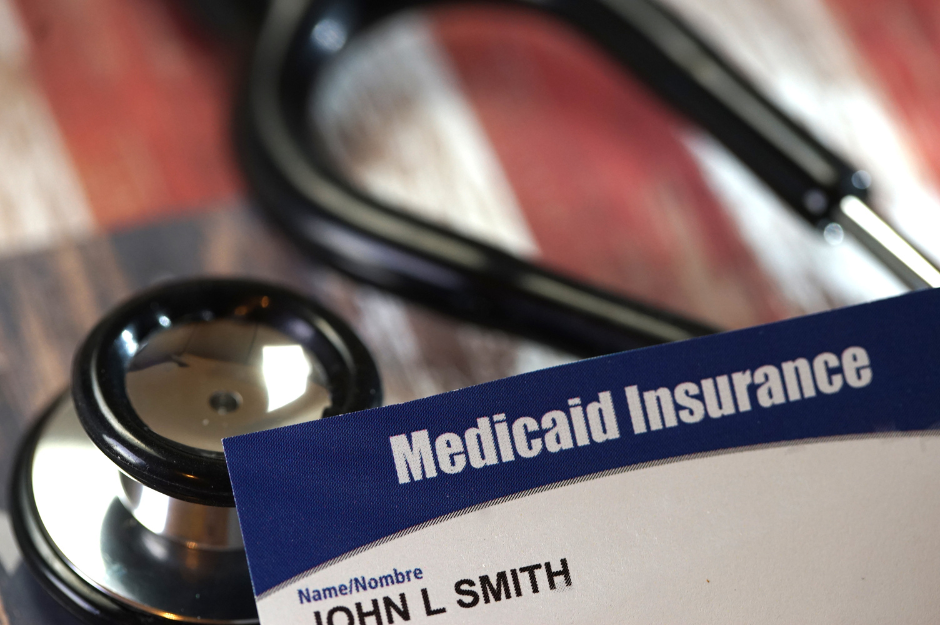 image contains a closeup of a stethoscope with a Medicaid Card in the foreground