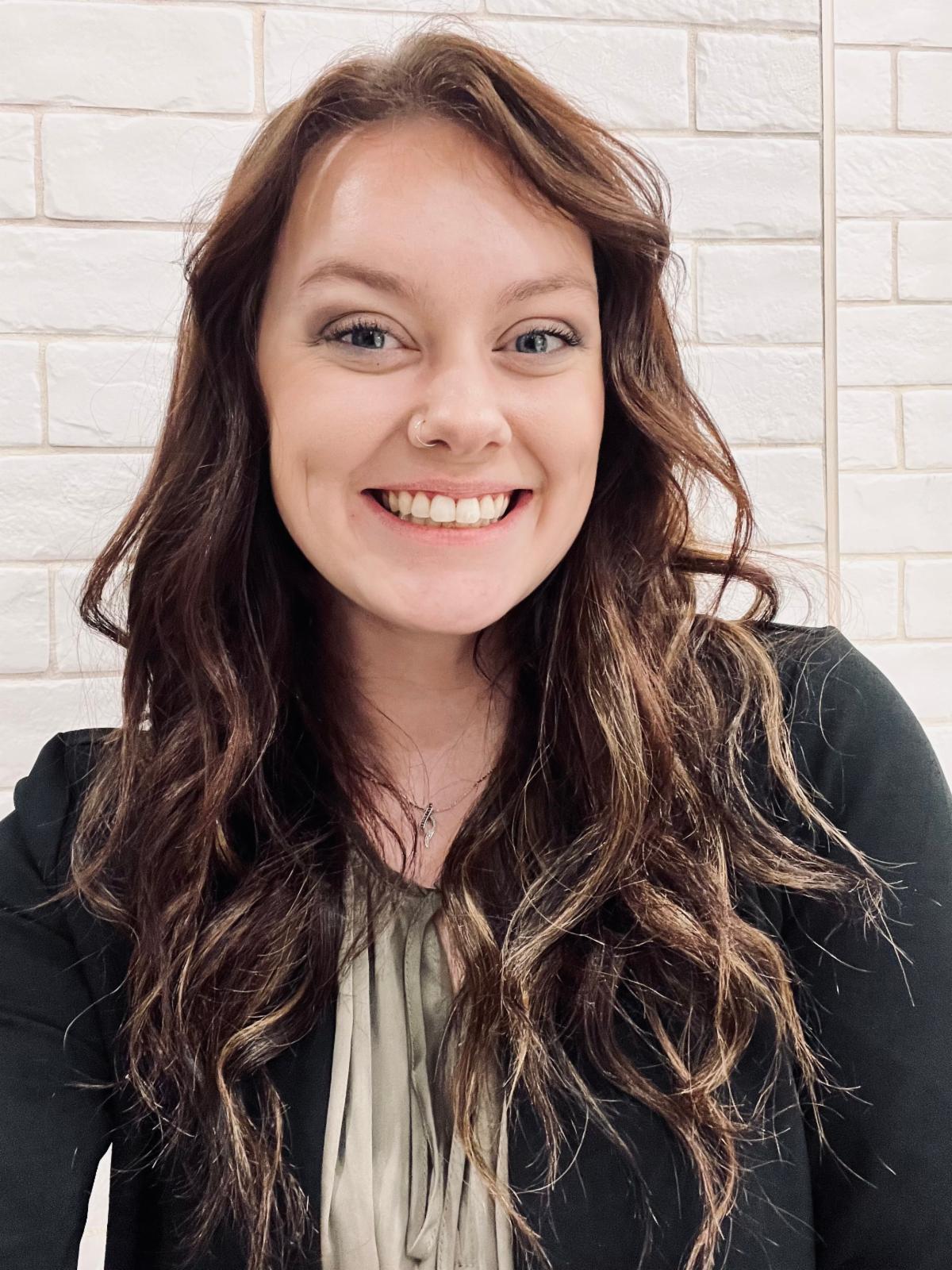 Female with long dark hair wearing a black cardigan and gray shirt looking at the camera and smiling