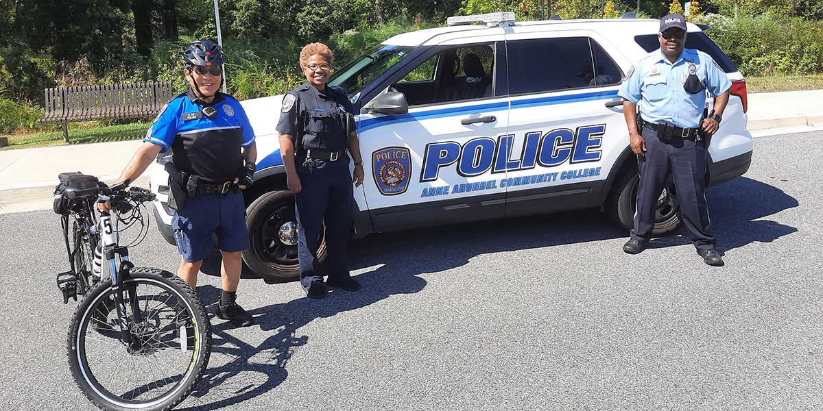 Three AACC officers poised beside a bicycle and a cruise vehicle.