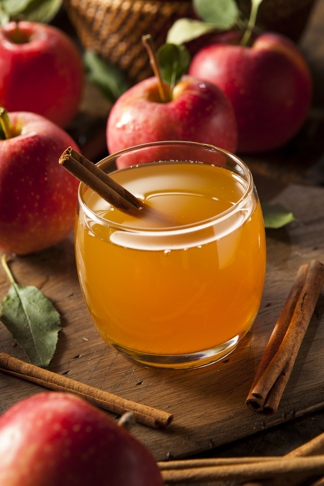 a glass of apple cider with a cinnamon stick surrounded by whole apples