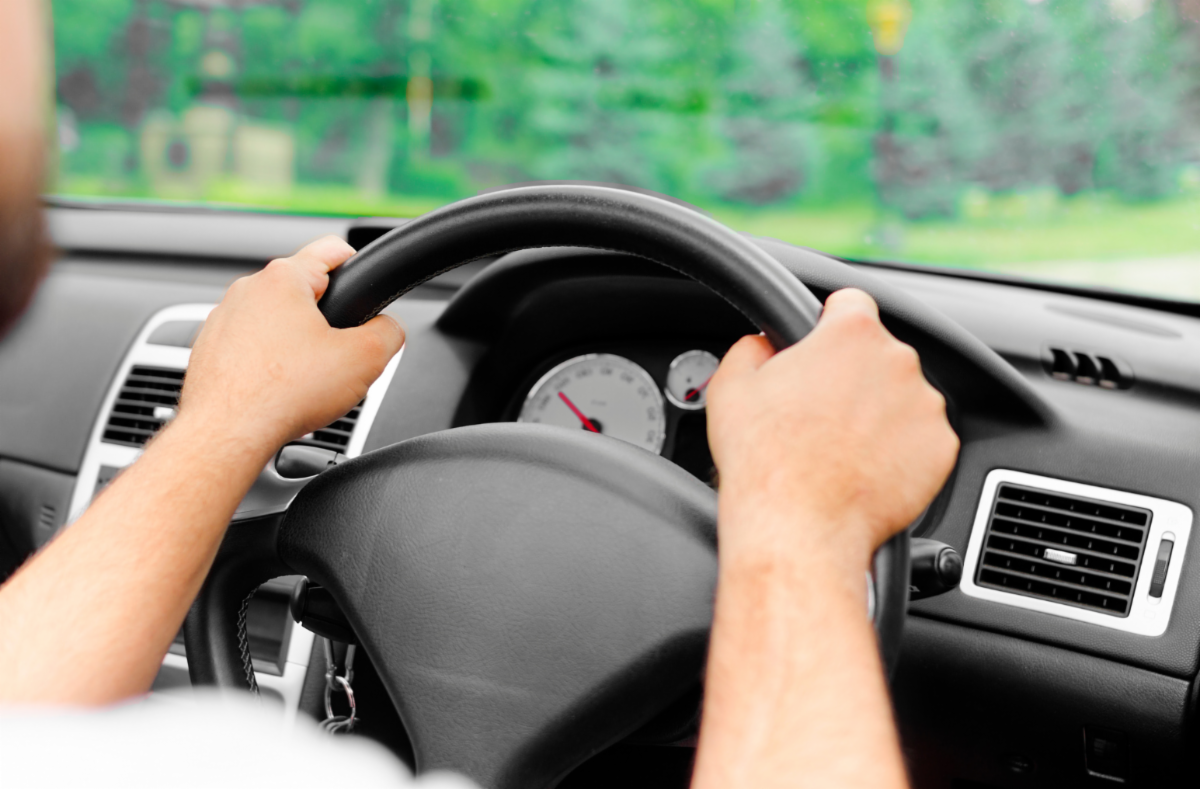 A person holding a steering wheel at the 10 and 2 position.