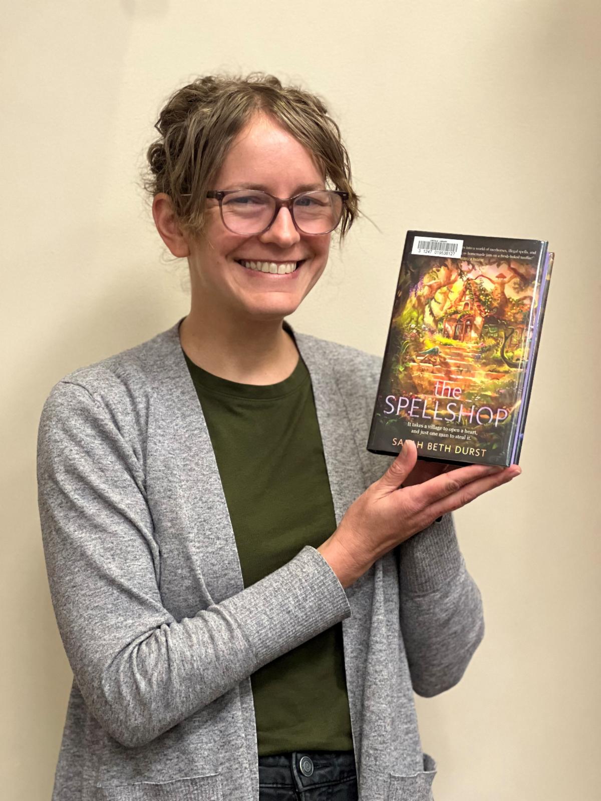 Woman in a cardigan holding a copy of The Spellshop