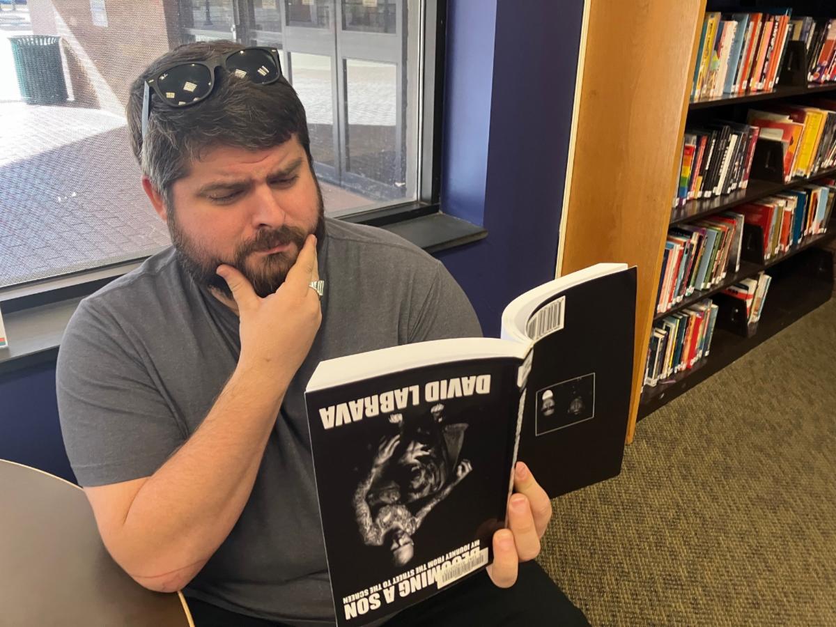 A man grasping his chin thoughtfully while holding Becoming a Son by David Labrava