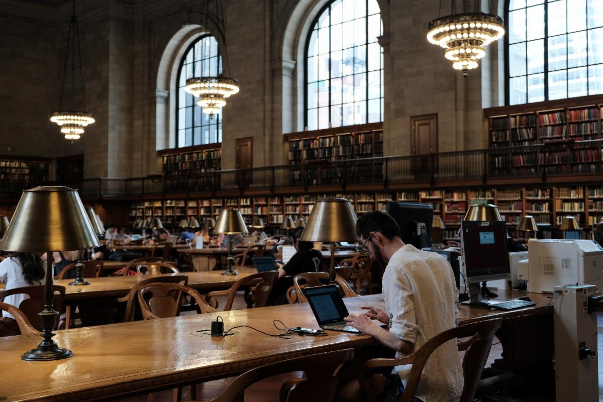 A man sits at a desk working on a laptop at New York Public Library. Photo by Calvin Uy on Unsplash.