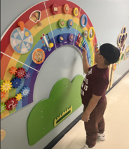 Boy with dark hair and brown t-shirt moving tactile objects around a rainbow on the wall