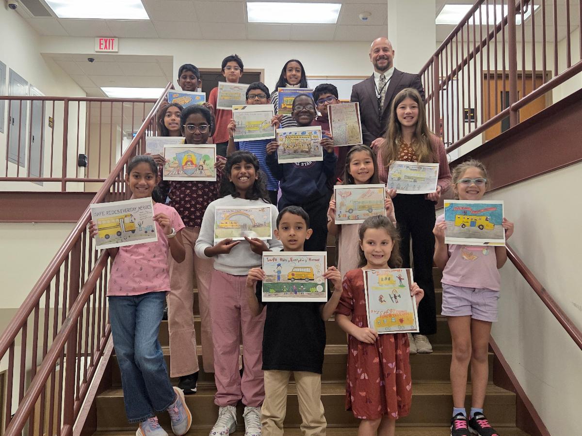 A group of North Allegheny students and a male administrator pose on a staircase holding up their winning school bus safety posters.