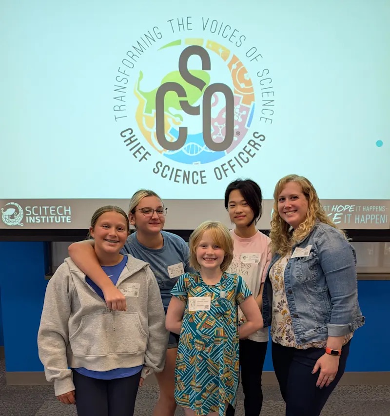 Carson Middle School students Stella Armstrong, Madi Dailey, Caroline Gao, and Gwendolyn Gassert pose with teacher advisor Laura Pacini in front of a Chief Science Officers display screen.