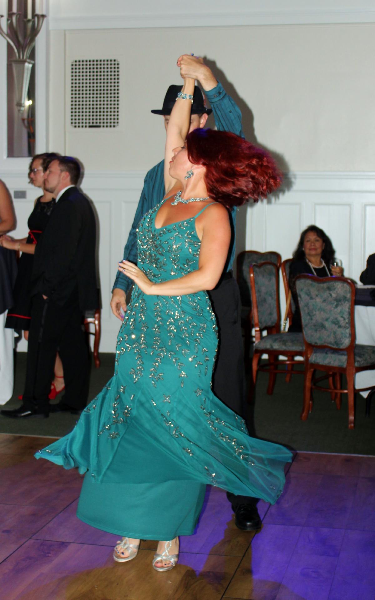 Man in black hat dancing with woman in turquoise gown with red hair streaming behind her
