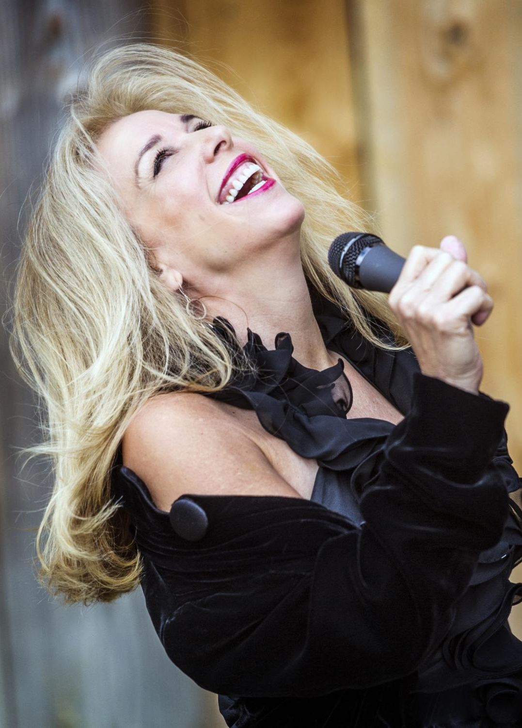 Jazz singer Amanda Carr, a smiling woman with long blonde hair holding a a microphone with her head thrown back