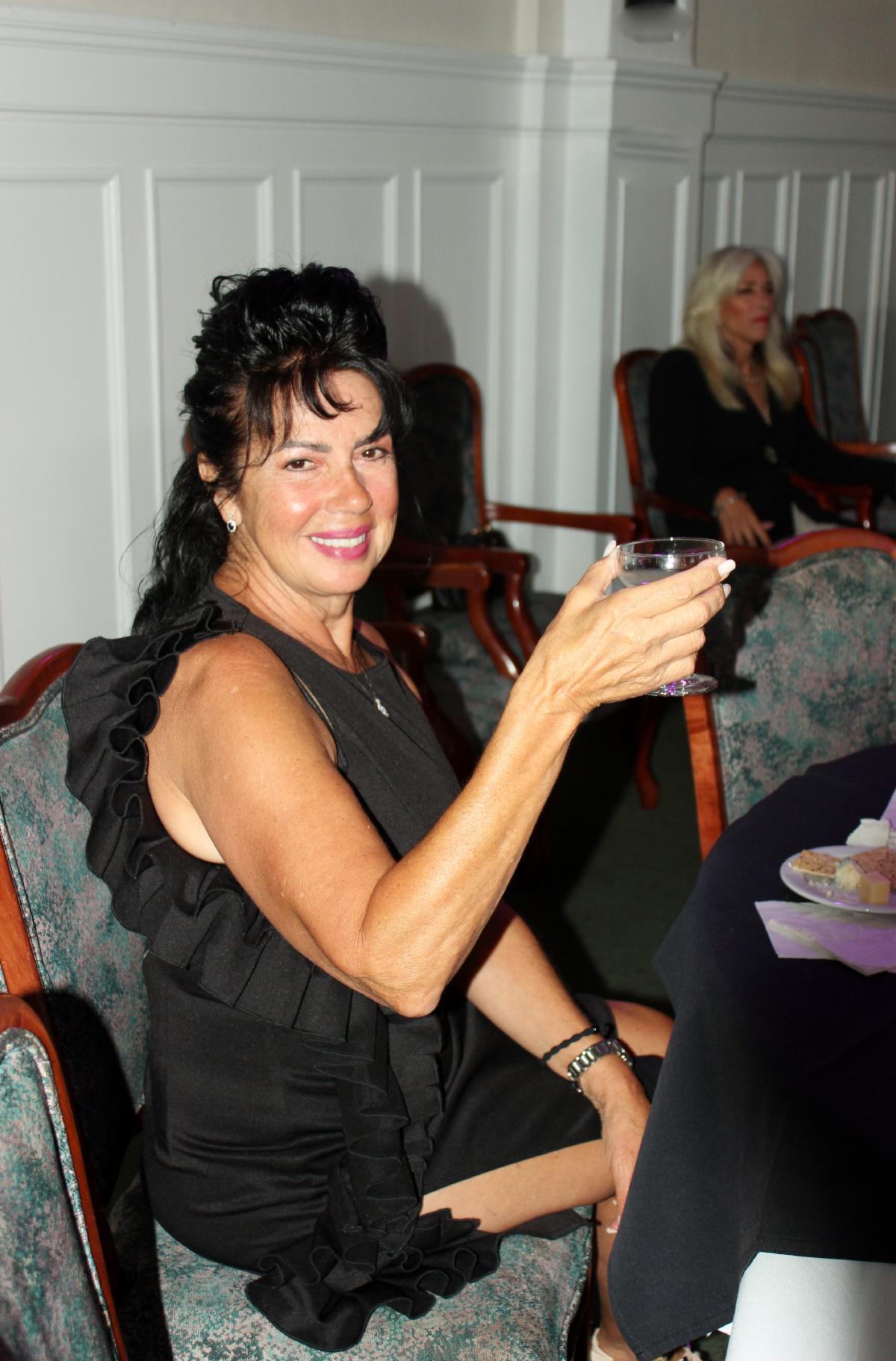 Smiling woman in sleeveless black dress raising a glass