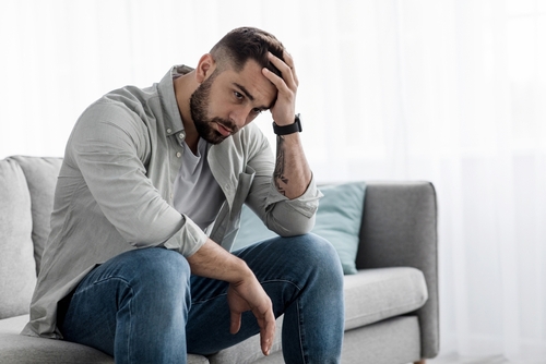 Man sit alone feeling sad worry regret or fear_ depressed and desperate in sofa at home. Suffering emotional pain and unhappy_ mental health. Young european handsome guy presses hand to forehead