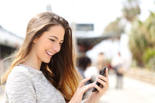 Happy girl texting on a smart phone in a train station while is waiting
