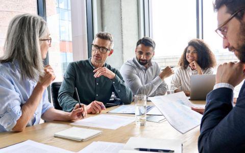 Group of people talking around a boardroom table. Papers on desk