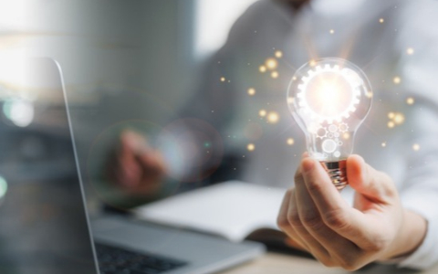 Abstract image of business person using laptop and holding a lightbulb in their left hand