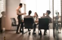 group of people seated around a board table while someone gives a presentation. Blurred image