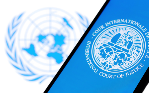 The image displays the emblem of the International Court of Justice placed on a blue background Behind the emblem is the logo of the United Nations which features a world map surrounded by olive branches There are no other elements text or symbols in the image and no people are present