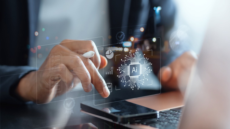 a person in a suit uses a stylus to interact with a transparent digital interface displaying various icons and graphs including a central icon of an AI chip the person is working on a laptop with a smartphone placed nearby