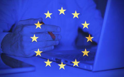 Hands using a laptop overlaid with the European Union flag stars symbolising EU regulation and digital policy.