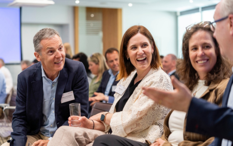 Three people seated in an audience talking together and laughing