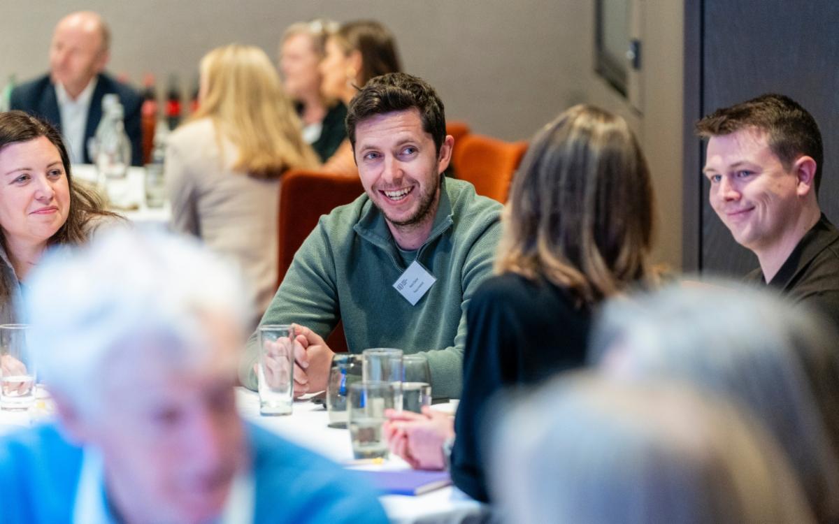 group of people sitting at a round table at an event talking and smiling