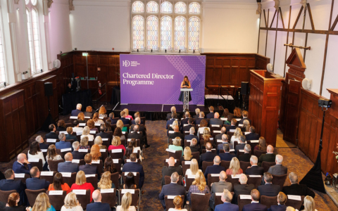 audience seated in two rows watching the speaker at the podium. Background signage says Chartered Director programme on purple banner