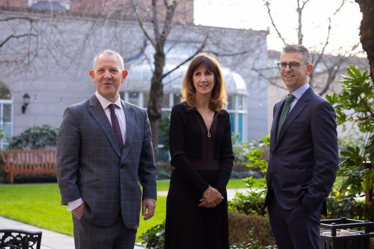 Three professionals standing together for a posed shot outdoors in a landscaped courtyard setting with buildings in the background.