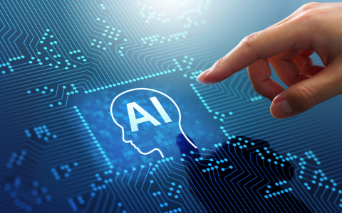 Illustration of a human hand pointing towards a digital icon of a human head containing the letters AI. The image features a blue, technology themed background with circuit patterns representing artificial intelligence and data networks.