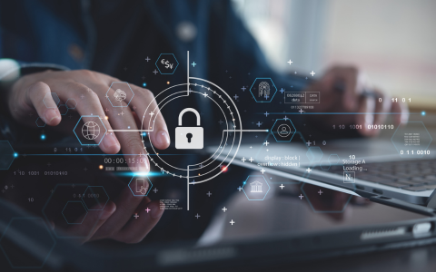 Abstract image of close up of hands on a laptop. The image is overlaid with a cybersecurity lock icon