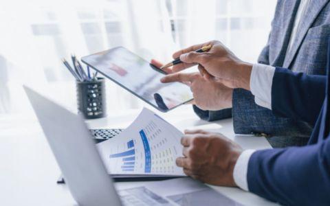 Hands with paperwork and a laptop and pen pointing to a laptop screen