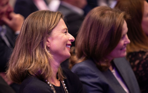 Two seated audience members listing and smiling. Dressed in business attire
