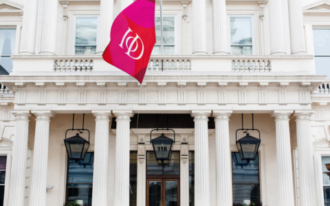 large white neoclassical building with tall columns red flag with white letters iod above entrance number 116 above door