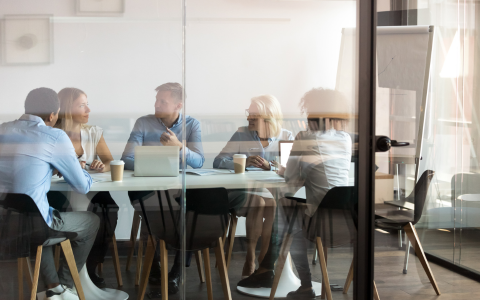 group of people seated around a boardroom table. Behind a glass window.
